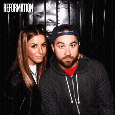 A Man And A Woman Are Posing For A Photo In Front Of A Wall That Says " Reformation " GIF