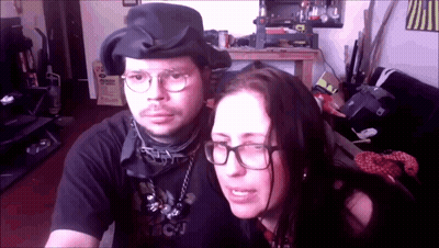 A Man And A Woman Are Posing For A Picture And The Woman Is Wearing Glasses And A Black Shirt That Says Bcj GIF