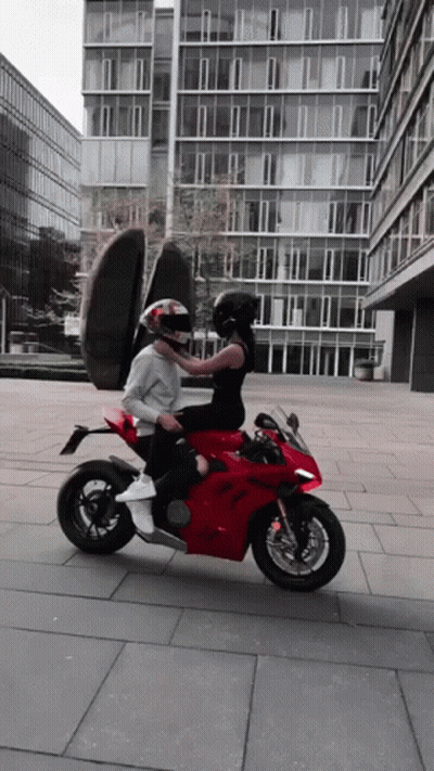 A Man And A Woman Are Riding A Red Motorcycle In Front Of A Building GIF