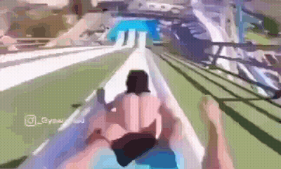 A Man And A Woman Are Riding Down A Water Slide At A Water Park . GIF
