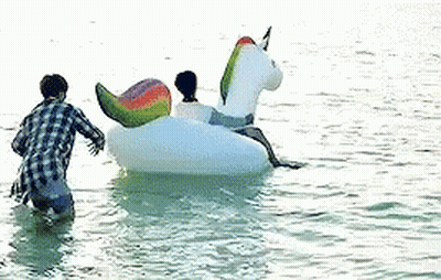 A Man And A Woman Are Riding On A Unicorn Float In The Water . GIF
