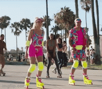 A Man And A Woman Are Rollerblading On A Street With Palm Trees In The Background .. GIF