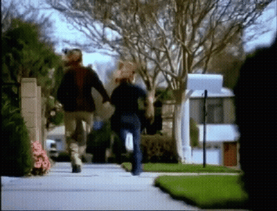 A Man And A Woman Are Running Down A Street Holding Hands . GIF