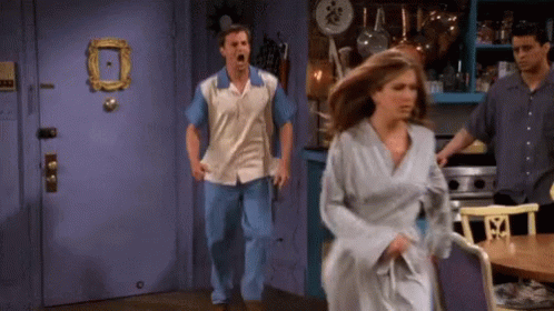 A Man And A Woman Are Running In A Kitchen With A Picture Frame On The Door GIF