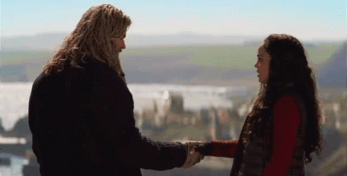 A Man And A Woman Are Shaking Hands In Front Of A Mountain Range . GIF