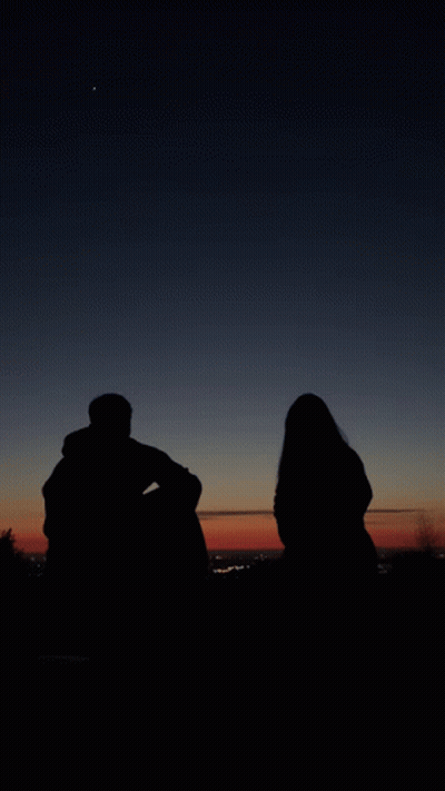A Man And A Woman Are Silhouetted Against A Dark Sky GIF