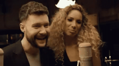 A Man And A Woman Are Singing Into A Microphone . GIF