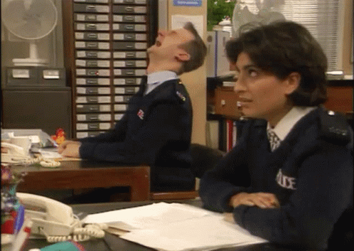A Man And A Woman Are Sitting At A Desk In A Police Office . GIF