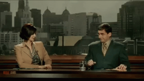 A Man And A Woman Are Sitting At A Desk With A Sign That Says ' News And ' GIF