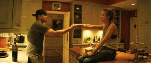 A Man And A Woman Are Sitting At A Kitchen Counter Holding Hands GIF