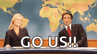 A Man And A Woman Are Sitting At A News Desk With The Words `` Go Us '' Written In Front Of Them . GIF