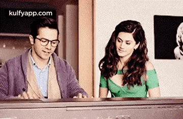 A Man And A Woman Are Sitting At A Piano And Looking At Each Other . GIF