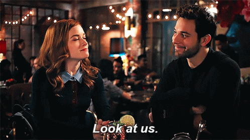 A Man And A Woman Are Sitting At A Table In A Restaurant And The Man Is Saying Look At Us GIF