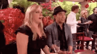 A Man And A Woman Are Sitting At A Table In A Restaurant . The Woman Is Wearing A Hat . GIF