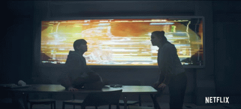 A Man And A Woman Are Sitting At A Table In Front Of A Netflix Sign GIF