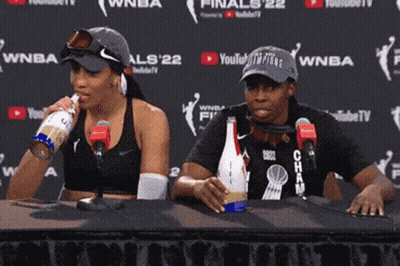 A Man And A Woman Are Sitting At A Table In Front Of Microphones And A Wall That Says Youtube Tv GIF