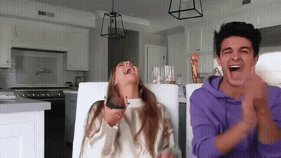 A Man And A Woman Are Sitting At A Table Laughing And Clapping In A Kitchen . GIF
