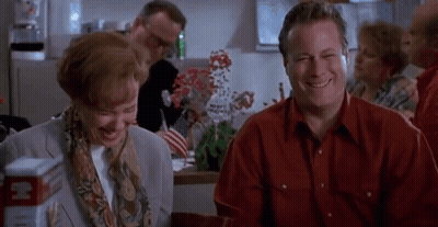 A Man And A Woman Are Sitting At A Table Laughing And Smiling . GIF