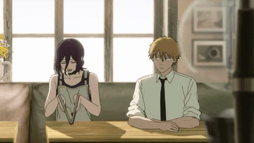A Man And A Woman Are Sitting At A Table Looking At Something . GIF