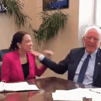 A Man And A Woman Are Sitting At A Table Shaking Hands . The Woman Is Wearing A Pink Jacket . GIF