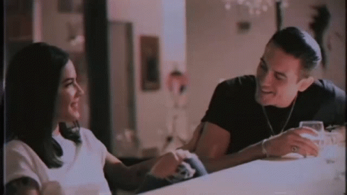 A Man And A Woman Are Sitting At A Table Talking To Each Other And Smiling . GIF