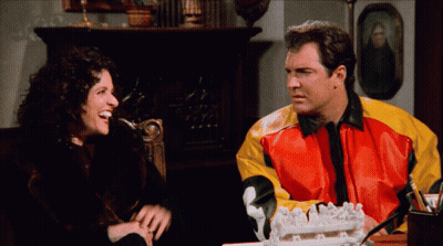A Man And A Woman Are Sitting At A Table With A Cake In Front Of Them GIF