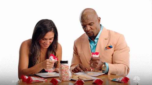 A Man And A Woman Are Sitting At A Table With A Jar Of Sprinkles On It GIF