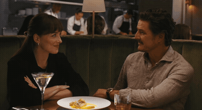 A Man And A Woman Are Sitting At A Table With A Martini GIF