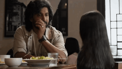 A Man And A Woman Are Sitting At A Table With A Plate Of Food GIF
