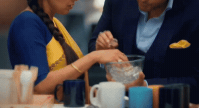 A Man And A Woman Are Sitting At A Table With Cups On It GIF