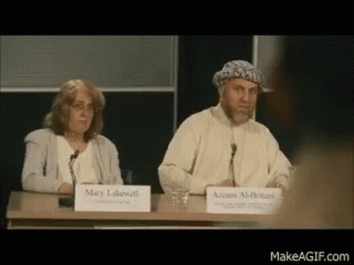 A Man And A Woman Are Sitting At A Table With Signs That Say Mary Lakewell And Azzam Al-Britanni GIF