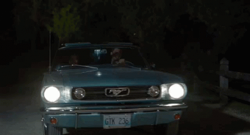 A Man And A Woman Are Sitting In A Blue Car At Night GIF
