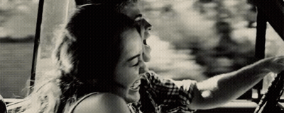 A Man And A Woman Are Sitting In A Car And Laughing . GIF