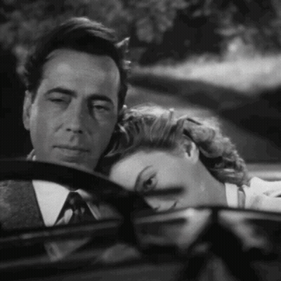A Man And A Woman Are Sitting In A Car And The Woman Is Resting Her Head On The Man 'S Steering Wheel GIF