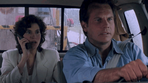 A Man And A Woman Are Sitting In A Car And The Woman Is Talking On Her Phone GIF
