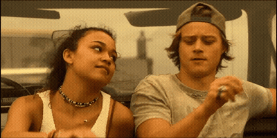 A Man And A Woman Are Sitting In A Car And The Woman Is Wearing A Necklace GIF