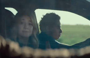 A Man And A Woman Are Sitting In A Car With A Field In The Background . GIF