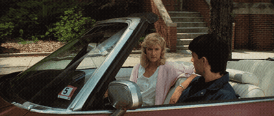 A Man And A Woman Are Sitting In A Car With A Sticker That Says S On It GIF