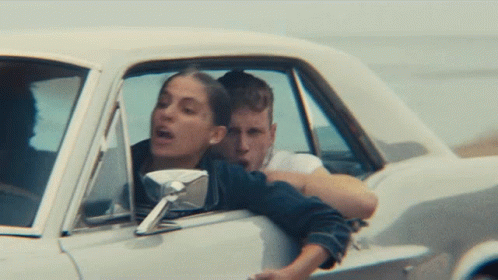 A Man And A Woman Are Sitting In A Car With The Woman Leaning Out The Window GIF