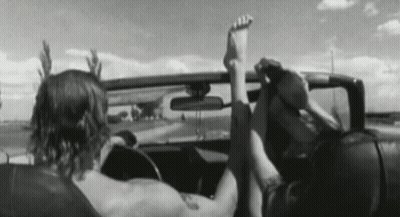 A Man And A Woman Are Sitting In A Car With Their Feet Up In The Air . GIF