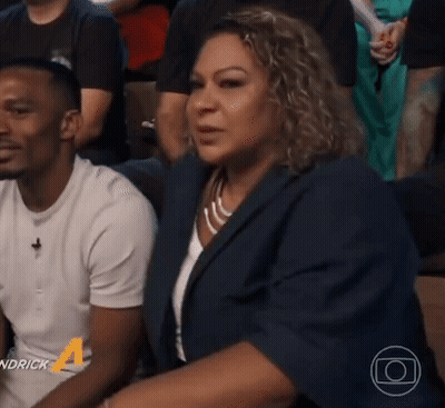 A Man And A Woman Are Sitting In A Crowd And The Man Is Wearing A White Shirt With The Number 4 On It GIF