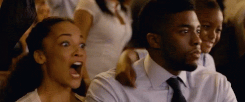 A Man And A Woman Are Sitting In A Crowd With Their Mouths Wide Open GIF