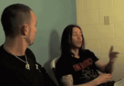 A Man And A Woman Are Sitting In A Room And The Man Is Wearing A Black Shirt That Says ' I ' GIF