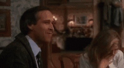A Man And A Woman Are Sitting In A Room With A Fire Coming Out Of A Fireplace . GIF
