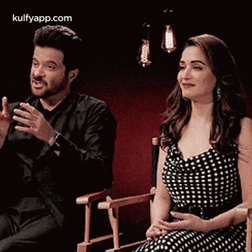A Man And A Woman Are Sitting In Chairs And Smiling . GIF