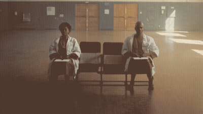 A Man And A Woman Are Sitting In Chairs Holding Signs That Say 9.4 GIF