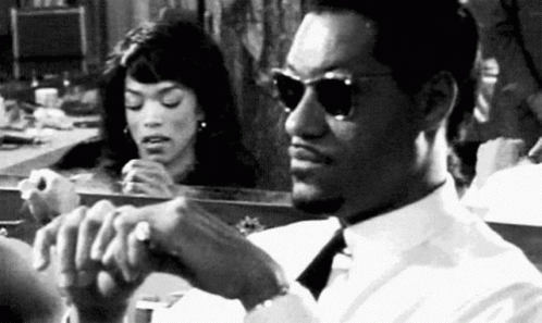 A Man And A Woman Are Sitting In Front Of A Mirror . The Man Is Wearing Sunglasses . GIF