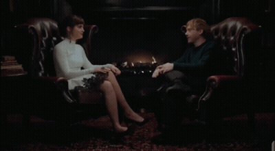A Man And A Woman Are Sitting In Leather Chairs Laughing GIF
