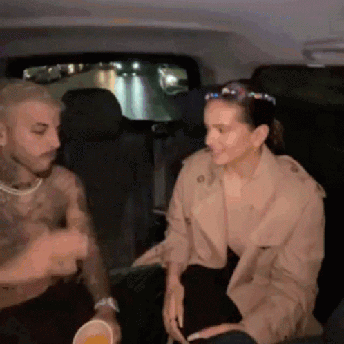 A Man And A Woman Are Sitting In The Back Seat Of A Car Talking GIF