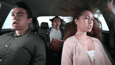 A Man And A Woman Are Sitting In The Back Seat Of A Car With Popcorn In Their Mouths GIF